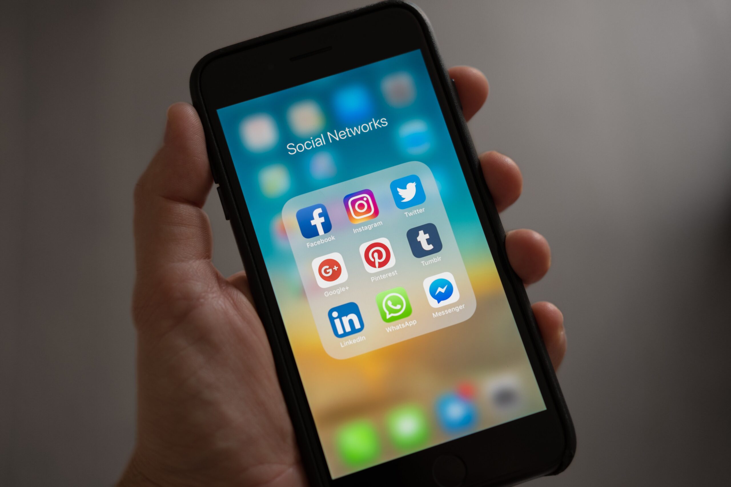 Close-up of a hand holding a phone with displayed app icons including Facebook, Instagram, WhatsApp, Messenger, Tumblr, Google+, Pinterest, LinkedIn, and Twitter, representing a diverse array of social media platforms.